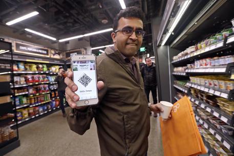 Amazon employee Krishna Iyer shows off an Amazon Go app as he shops in the store, Monday, Jan. 22, 2018, in Seattle. The store allows shoppers to scan their smartphone with the Amazon Go app at a turnstile, pick out the items they want and leave. The online retail giant can tell what people have purchased and automatically charges their Amazon account. (ANSA/AP Photo/Elaine Thompson) [CopyrightNotice: Copyright 2018 The Associated Press. All rights reserved.]