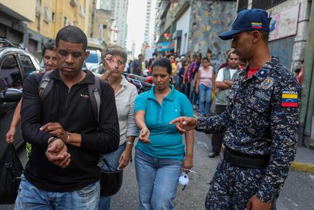 epa06967525 An officer of the Bolivarian National Police (R) checks stamps on peoples arms after they were authorized to make purchases at a market in Caracas, Venezuela, 23 August 2018. Hundreds of Venezuelan police officers visited different kinds of shops to monitor compliance with the so-called 'fair prices' that the Government of Venezuelan President Nicolas Maduro recently set in the framework of his economic 'recovery' plan.  EPA/CRISTIAN HERNANDEZ