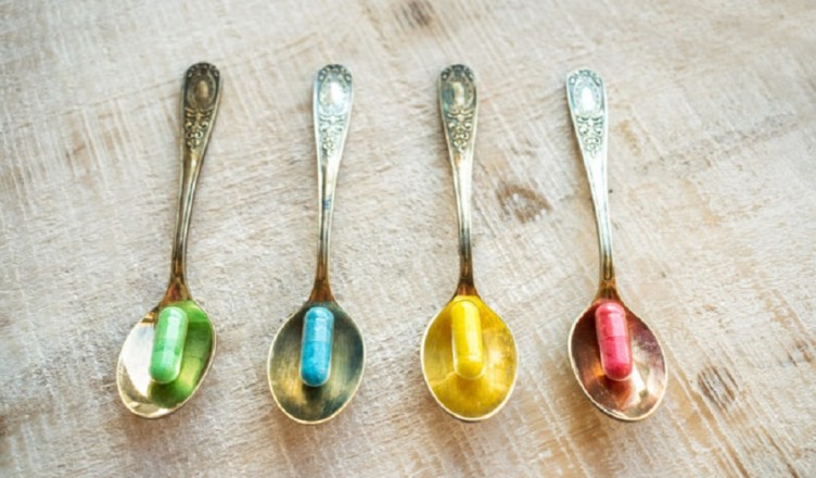 4 four multi-colored capsules (yellow, red, blue and green) in 4 vintage metal spoons on a wooden background. Different pills and drugs tablets. Pharmacy antibiotic antidepressant.