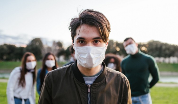 Group of teenagers friends at park wearing medical masks to protect from infections and diseases - Conceptual Coronavirus virus quarantine - Copy space - Multiracial people having fun together