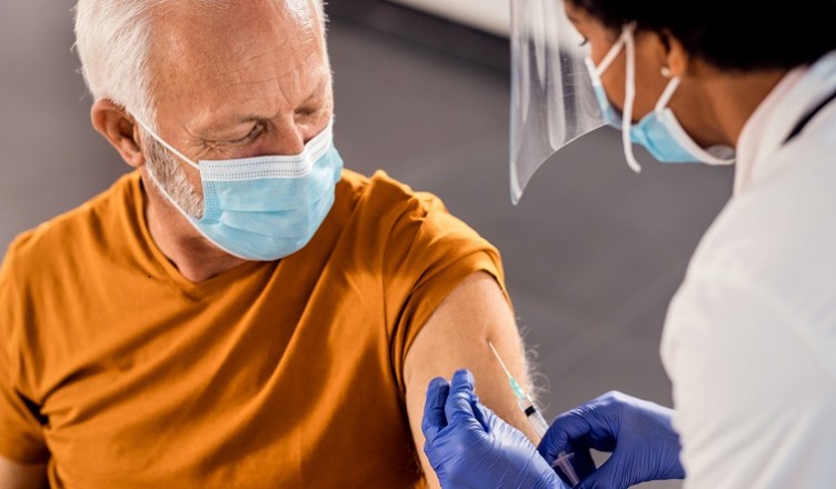 Senior man wearing face mask while receiving vaccine at medical clinic.