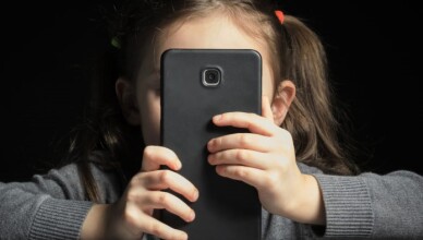 Problem of kids addiction to gadgets, online and screen time. Little girl with big smartphone in her hands.