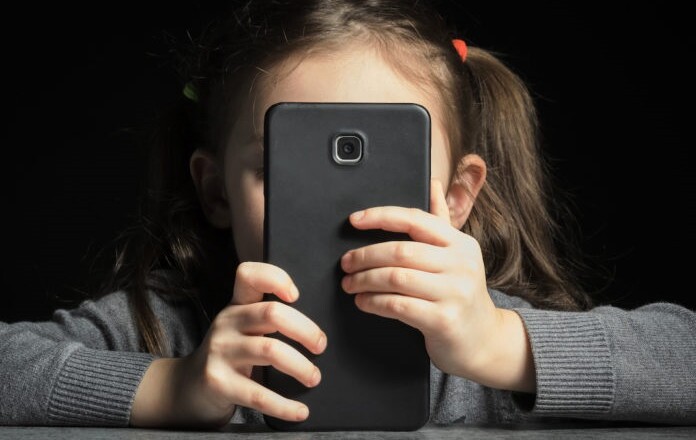 Problem of kids addiction to gadgets, online and screen time. Little girl with big smartphone in her hands.